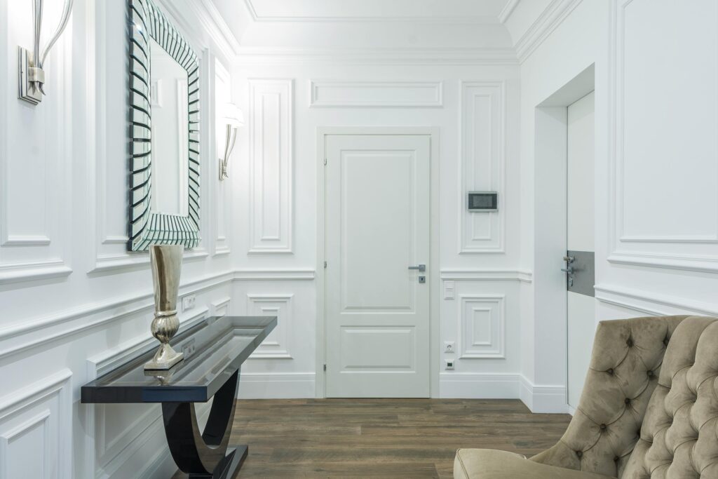 pexels photo 7598132 7598132 Sophisticated white interior with classic moldings and minimalist design, featuring a stylish mirrored wall and cozy seating.
